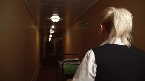 A maid rolls a trolley down the hall in the hotel and greets a man walking Stock-Footage 101227007