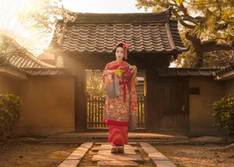 Maiko in a kimono posing on a stone path in front of the gate of a traditiona Stock Photos