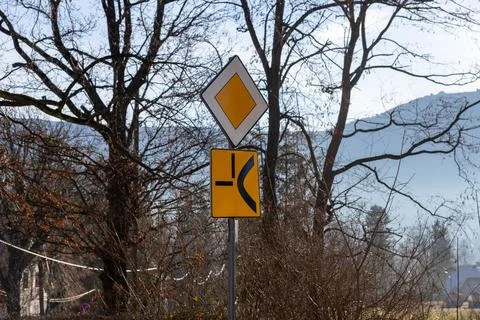 A main road sign with a priority indicator and a junction warning marker stands Фото