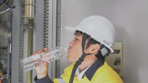 Maintenance technician is drinking water in front of the fire control cabinet. 스톡 동영상 129034196