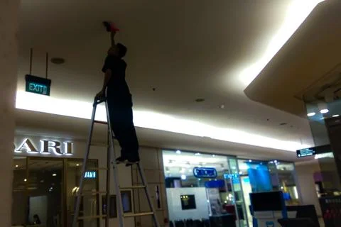 Maintenance Worker Cleaning Ceiling Light on Stepladder in Mall Stock Photos