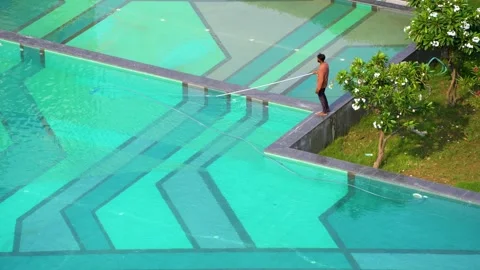 A maintenance worker cleaning a large swimming pool at a premium residential Stock Footage 337259845