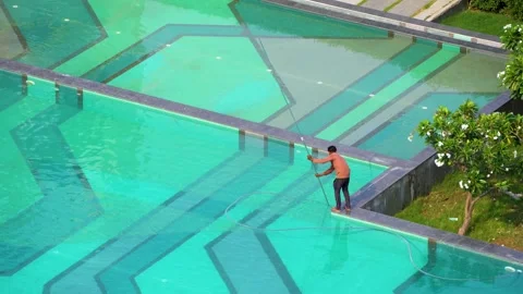 A maintenance worker cleaning a large swimming pool at a premium residential Stock Footage 337259885