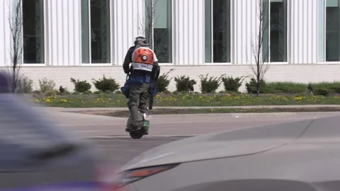 Maintenance worker rides unicycle cleaning parking lot with leaf blower Vídeos de archivo 152605317