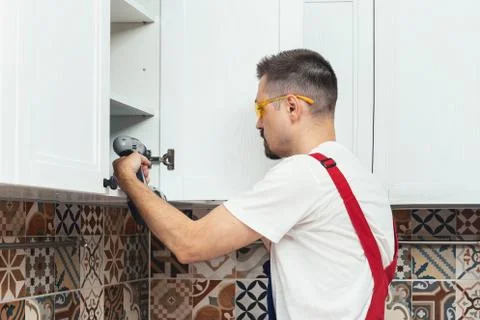 Maintenance worker using electric screwdriver while installing new furniture in Stock Photos