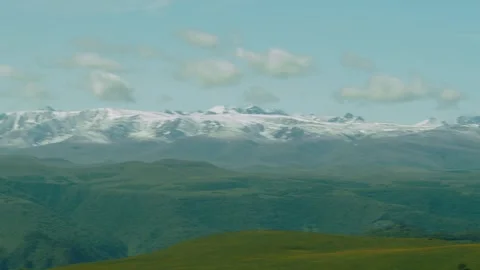 Majestic snow-capped mountain range rises above green hills in a vibrant natural Stock Footage 313107653