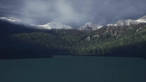 Majestic Snow Capped Mountain Range Behind Dense Green Forest and Calm Lake Stock Footage 338251284