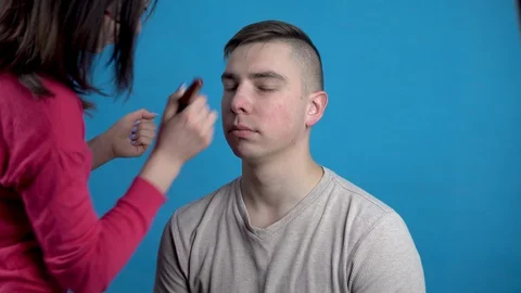 Make-up is applied to a young man. The girl applies makeup to a man before Stock Footage 128043591