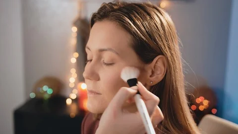 A make-up artist applies a blush with an average white brush on the face of a Stock Footage 101097715