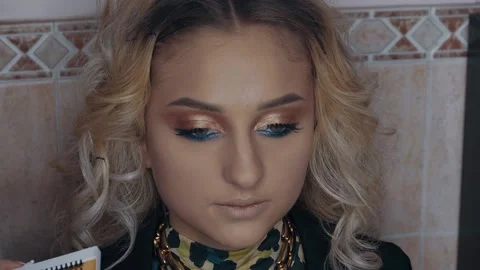 Make-up artist applies false eyelashes to confident blonde woman, filmed from Stock Footage 157456134