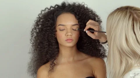 Make-up artist is applying eye shadows on face of beautiful dark haired model Video stock 88885541