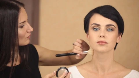 Make-up artist is applying a large powder brush to a beautiful young model Stock Footage 86992130