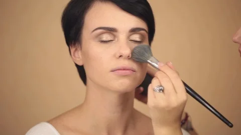 Make-up artist is applying a large powder brush to a beautiful young model Stock Footage 86992143