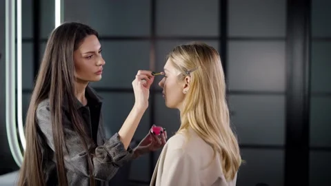 Make-up artist combs and styles the eyebrows of a young blonde woman in beauty Stock Footage 235659630