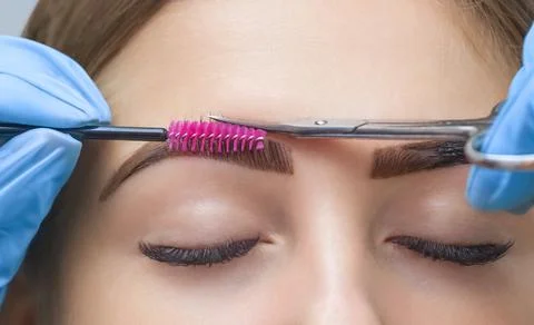 The make-up artist cuts her eyebrows with scissors. Stock Photos