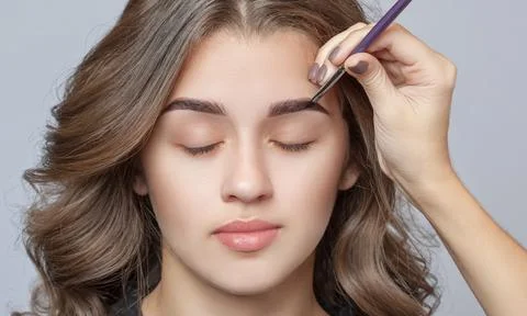 Make-up artist does eyebrow make-up to a woman with curly brown hair and nude Stock Photos