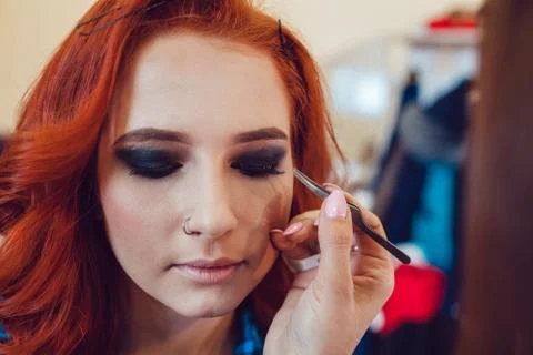 Make-up artist does makeup to the red-haired girl in studio. Smoky eyes Stock Photos