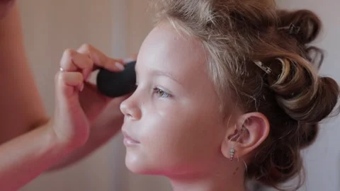 A make-up artist does professional makeup for a little girl, makes up before an Stock Footage 247416232