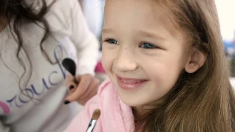 Make up artist doing make up with brush to smiling little girl in white salon Stock Footage 73908423
