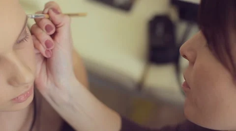 Make-up artist doing make-up of model, working with an area under the eyebrows Stock Footage 50358599