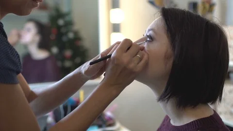 Make-up artist doing makeup and hair styling to a beautiful young woman Stock Footage 82639248