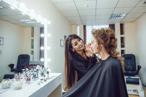 Make up artist doing professional makeup of young woman near the mirror in Stock Photos