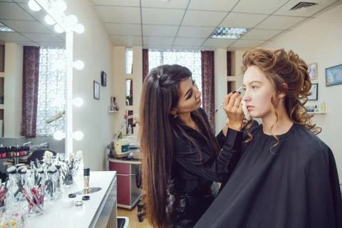 Make up artist doing professional makeup of young woman near the mirror in Stock Photos
