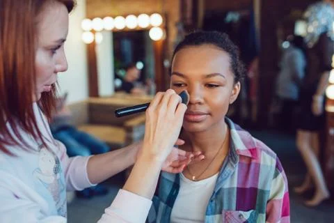 Make up artist doing professional makeup of young african woman in beauty studio Stock Photos