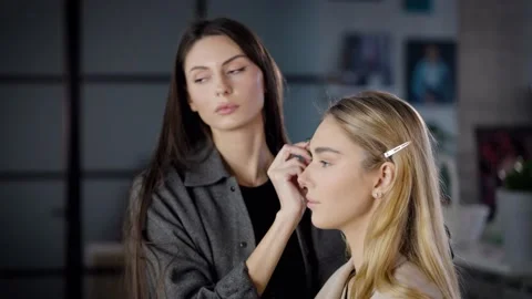 Make-up artist drawing eyebrows with an eyebrow pencil on a young blonde woman Stock Footage 236117417