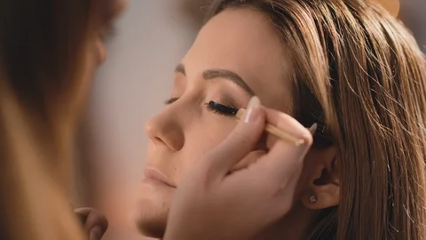 The make-up artist gently puts a black eyeliner on the eyelids of the eyes, with Stock Footage 101049789