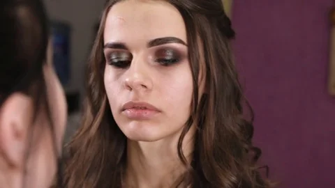 Make-up artist looks at the face of the model and puts shadows on her eyelids Stock Footage 84989144