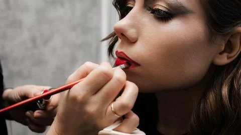 Make-up artist makes lip makeup art for a young girl in a beauty salon. Red l Stock Photos