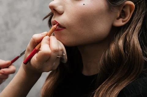 Make-up artist makes lip makeup art for a young girl in a beauty salon. Red Stock Photos