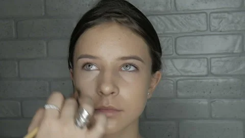 Make-up artist makes makeup to a young girl. Artist evens skin tone on model fac Stock Footage 102044179