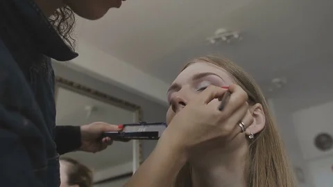 Make-up artist makes a professional make-up for a very beautiful girl in a photo 库存影片 76325902