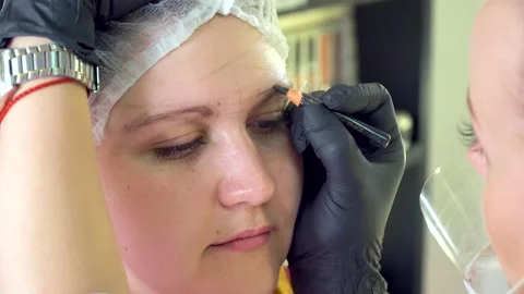 Make-up artist marks up client eyebrows in front of permanent makeup Stock Footage 153844235