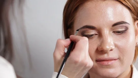 Make-up artist is painting over a brows of girl by brush and shadows Stock Footage 86112180