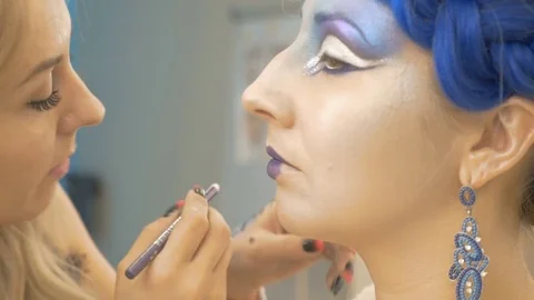 The make-up artist paints the lips of the model in purple. She creates a fairy Stock Footage 83659296