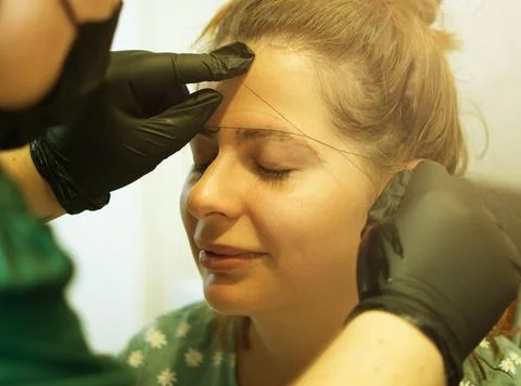 Make-up artist plucking eyebrows with a thread Professional face care. Stock Photos