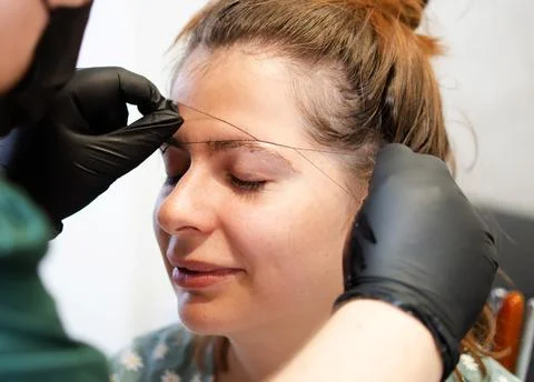Make-up artist plucking eyebrows with a thread Professional face care. Stock Photos