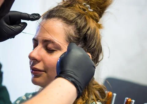 Make-up artist plucking eyebrows with a thread Professional face care. Stock Photos