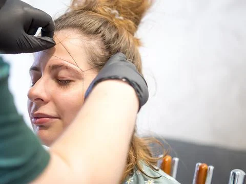 Make-up artist plucking eyebrows with a thread Professional face care. Stock Photos