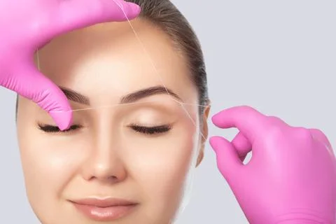 The make-up artist plucks eyebrows with a thread close-up. Women's cosmetolog Stock Photos