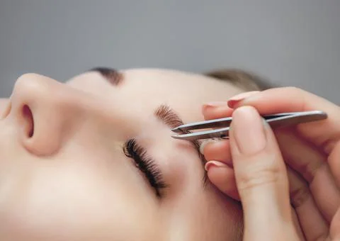 The make-up artist pulls out a pair of tweezers to a beautiful young girl in  Stock Photos