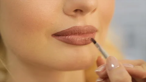 The make-up artist puts on the lips of the model a light lipstick Stock Footage 87634263