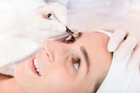 Make up artist working on woman's eyebrows in salon Stock Photos