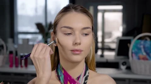 A make-up artist's hand applies foundation or sculptor with a brush to a young Stock Footage 236117690