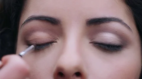 Make up artist's hand blending with a brush eyeshadow on girl's eye Video stock 74709442