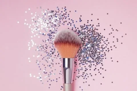 Make-up brush and star shaped confetti on pink backround, top view. Stock Photos