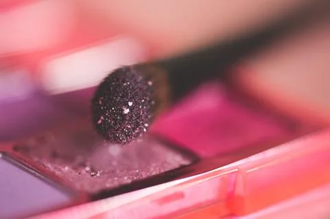 Make up brush with glitter eye shadow on in pink shade closeup. Selective foc Stock Photos